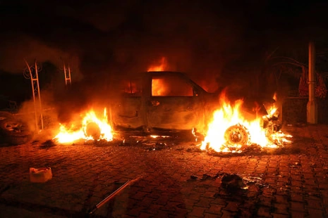 “A car engulfed in flames at night, with intense fire consuming the vehicle on a paved surface