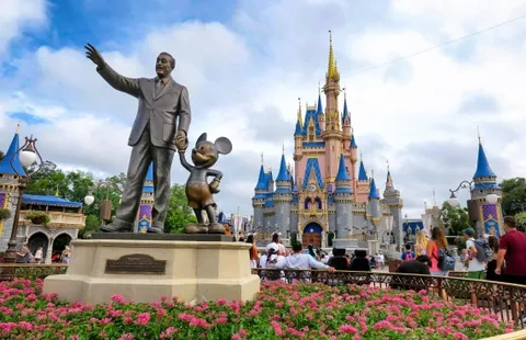 Statue of Walt Disney and Mickey Mouse in front of Cinderella Castle at Disney World's Magic Kingdom, with tourists taking pictures.