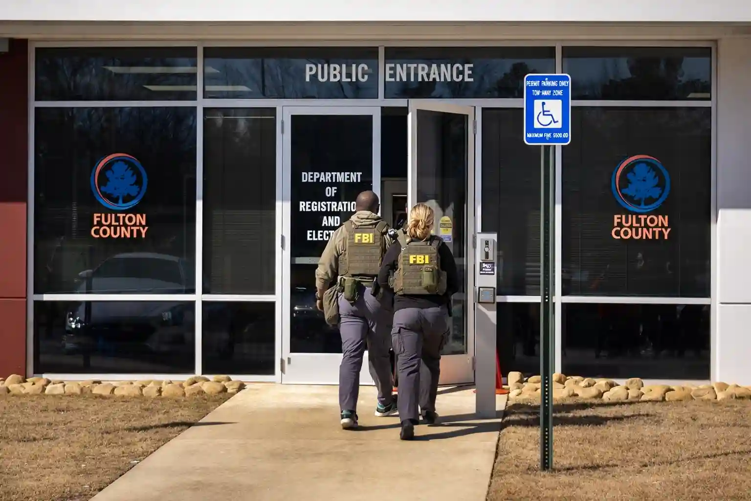FBI agents in tactical gear walking towards the entrance of a building marked with the Fulton County logo, as they prepare to execute a search warrant