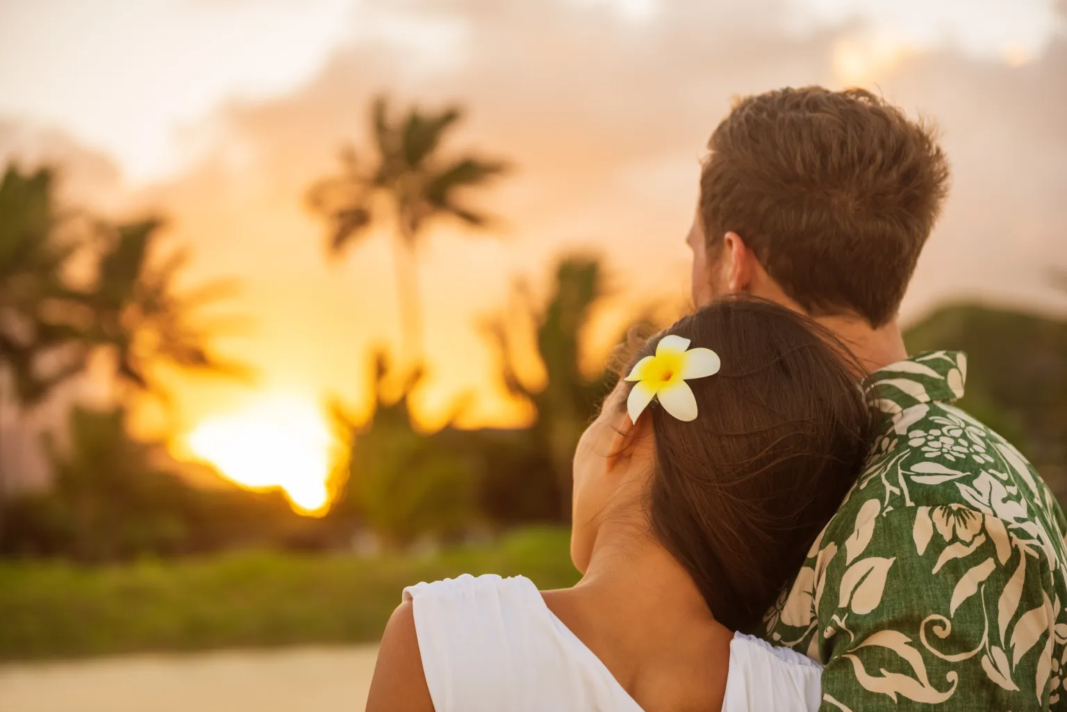 Couple watching sunset on a Hawaii beach with plumeria flower.
