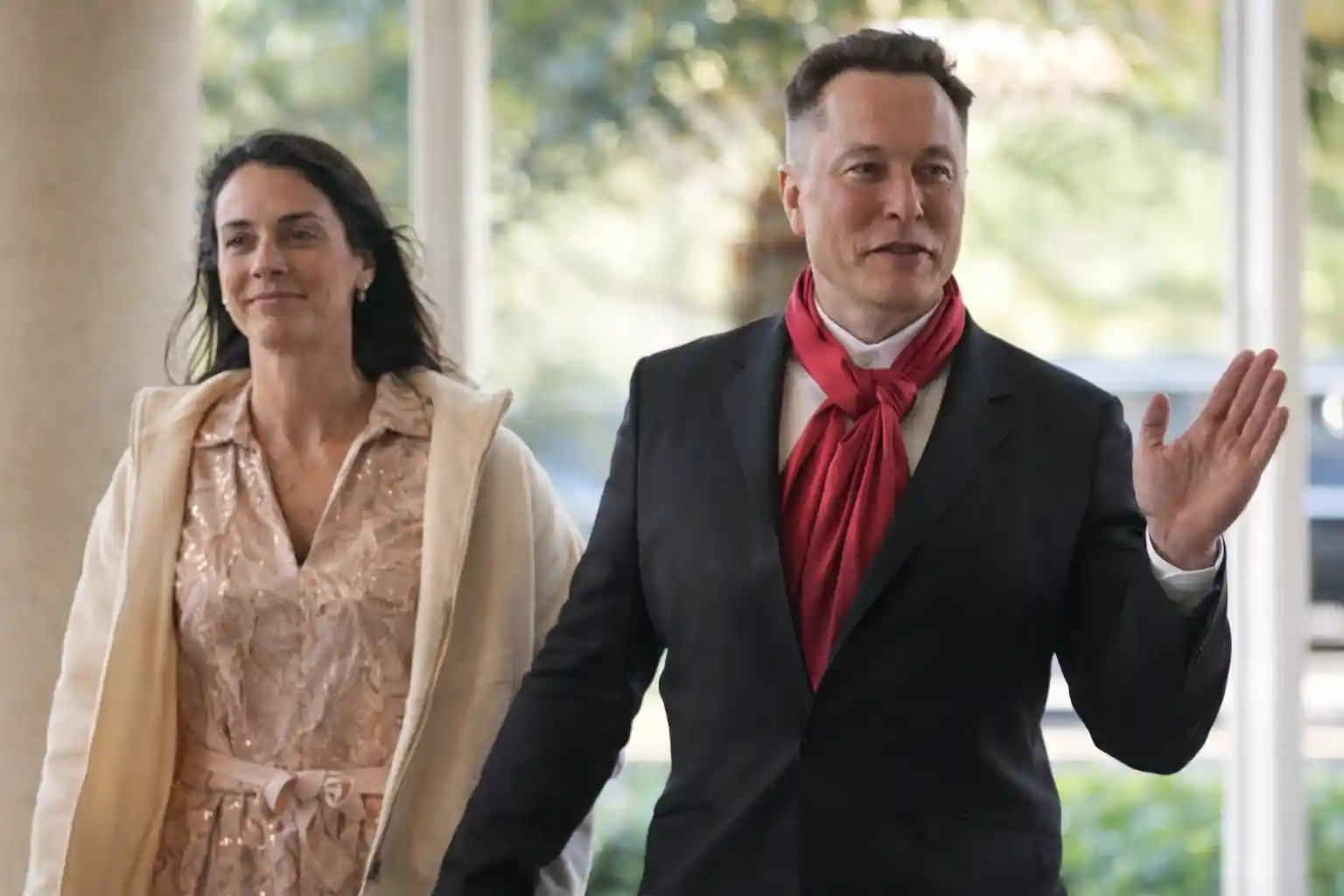Elon Musk walks with a companion while waving during a public appearance