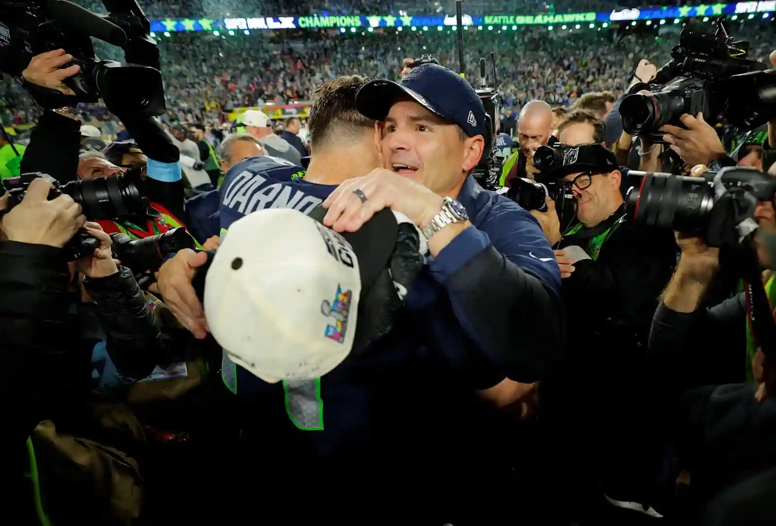 Seattle Seahawks head coach embraces quarterback Sam Darnold on the field as photographers capture the celebration after their Super Bowl LX victory