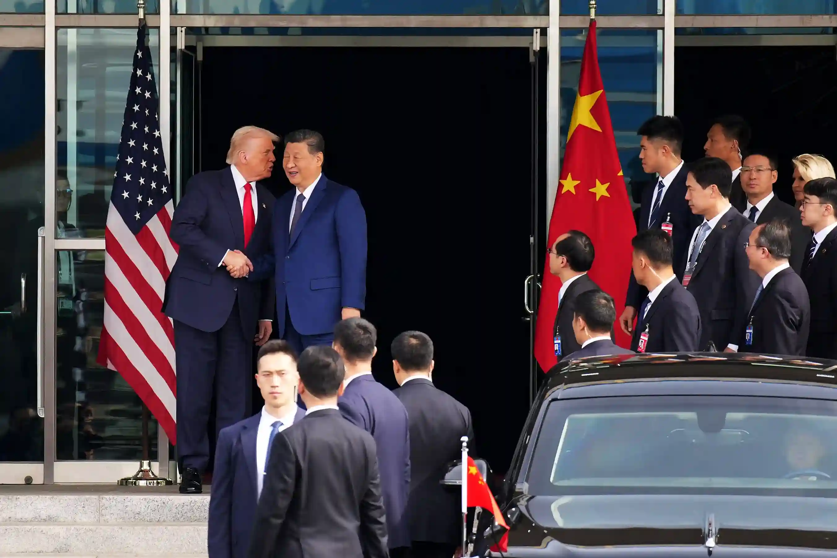 Donald Trump and Xi Jinping shake hands outside a building as aides and security look on.