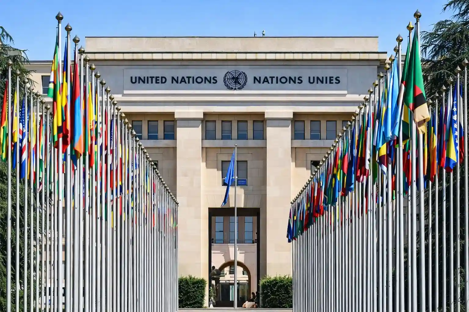 A wide shot of the United Nations headquarters in Geneva, with flags from various member states on display in front of the building.